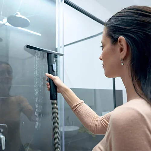 utilisation de la shampouineuse Hoover HS5 pour nettoyer une paroi de douche vitrée avec raclette