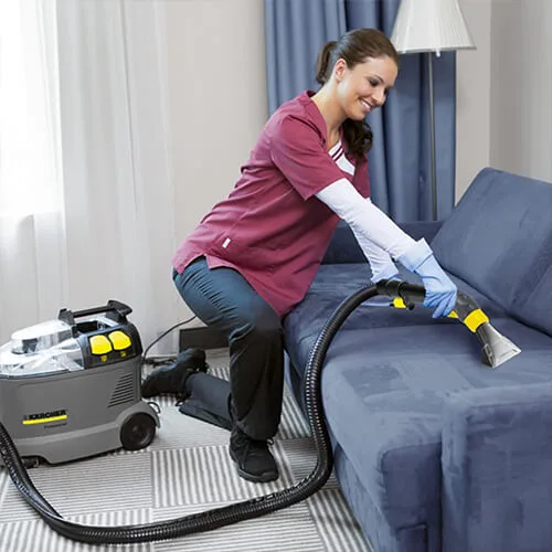 Nettoyage d’un canapé avec la shampouineuse Kärcher Puzzi 8/1 C par une professionnelle en uniforme